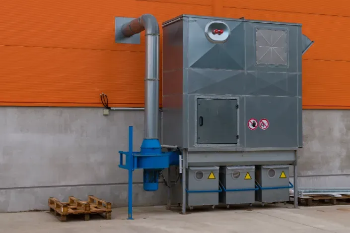 Industrial air filtration system, silver and blue, against an orange and gray building exterior.