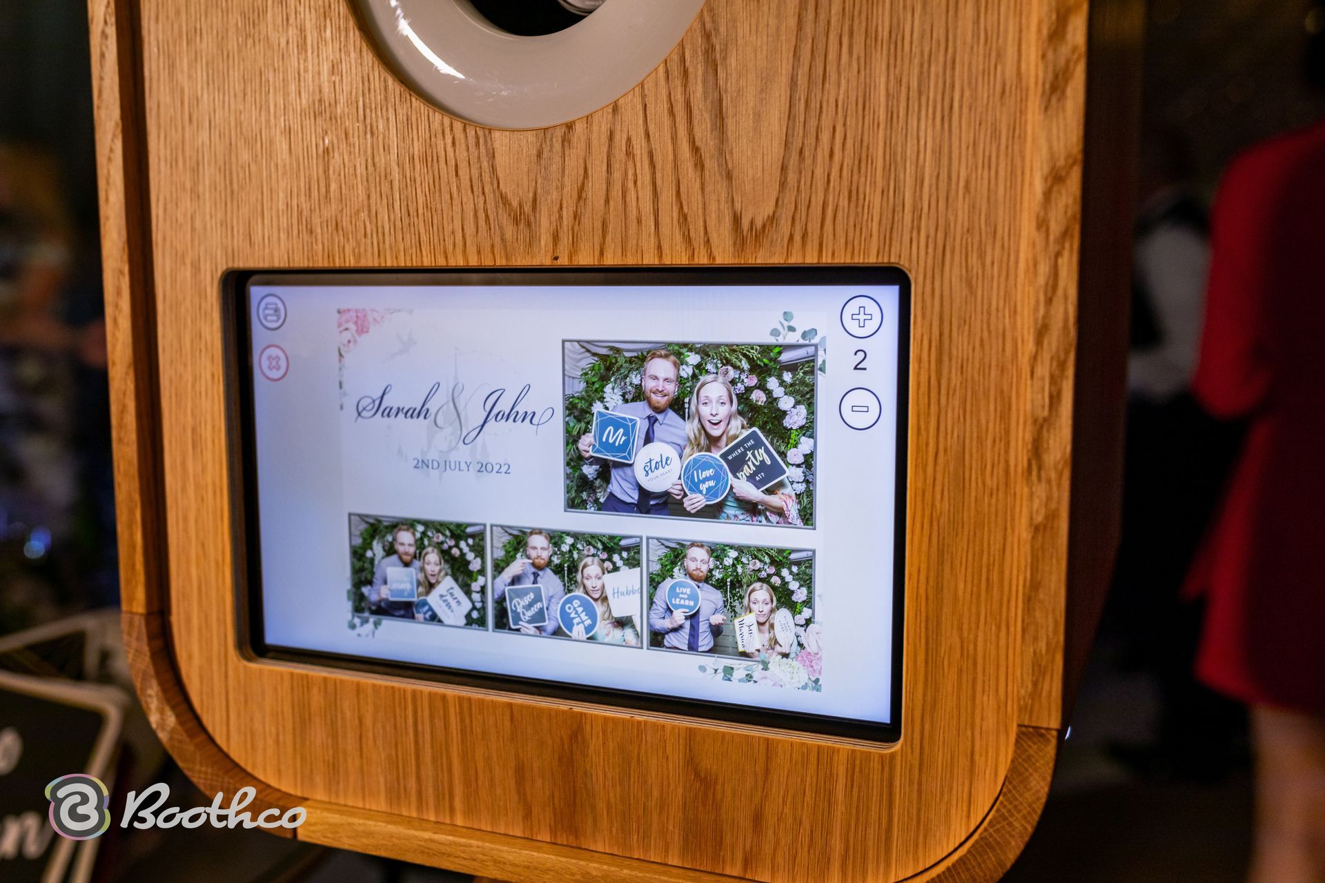 A wooden photo booth display showing a wedding photo strip featuring a couple posing with props.