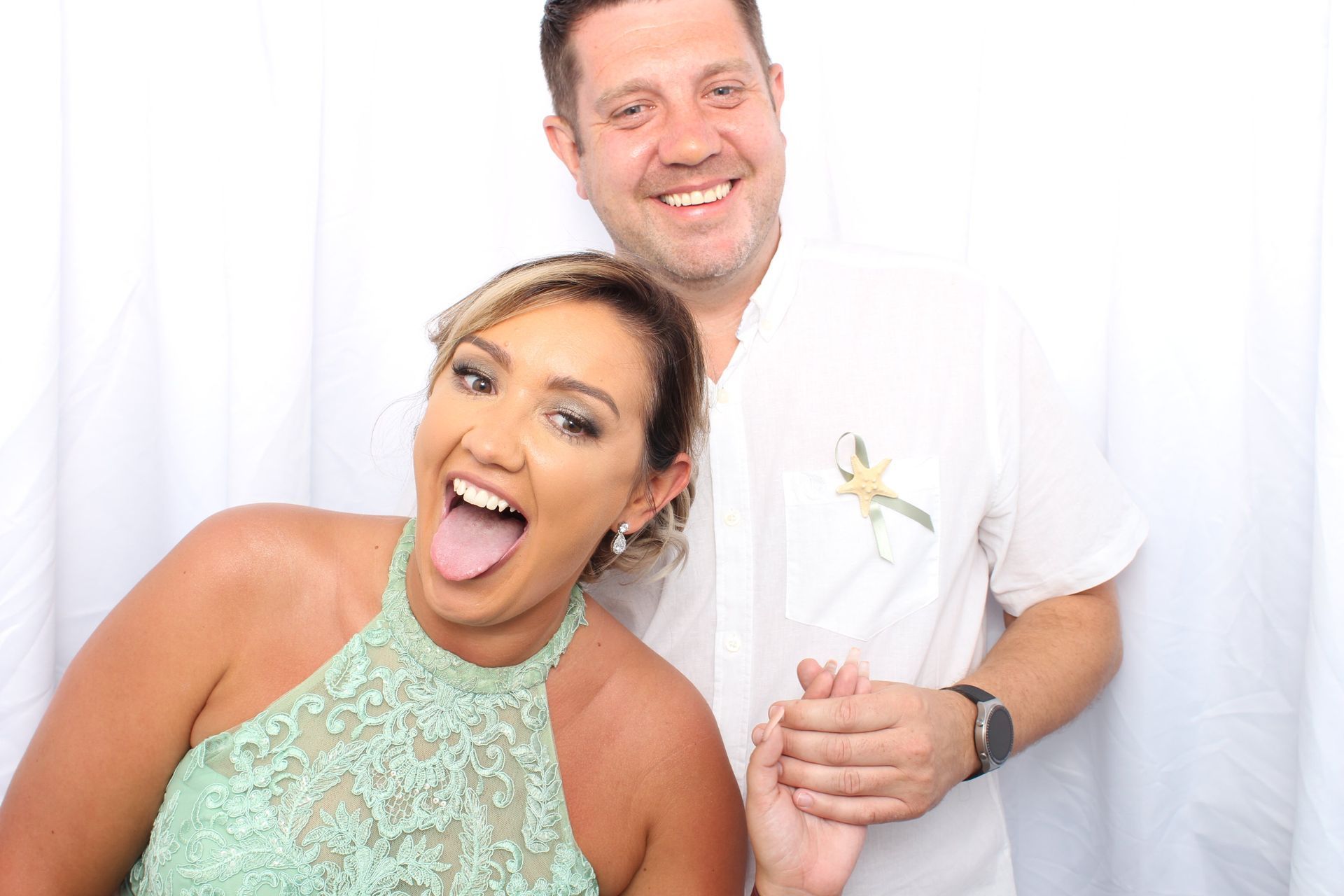 A woman in a green lace dress sticking her tongue out, posing next to a man in a white shirt holding her hand.