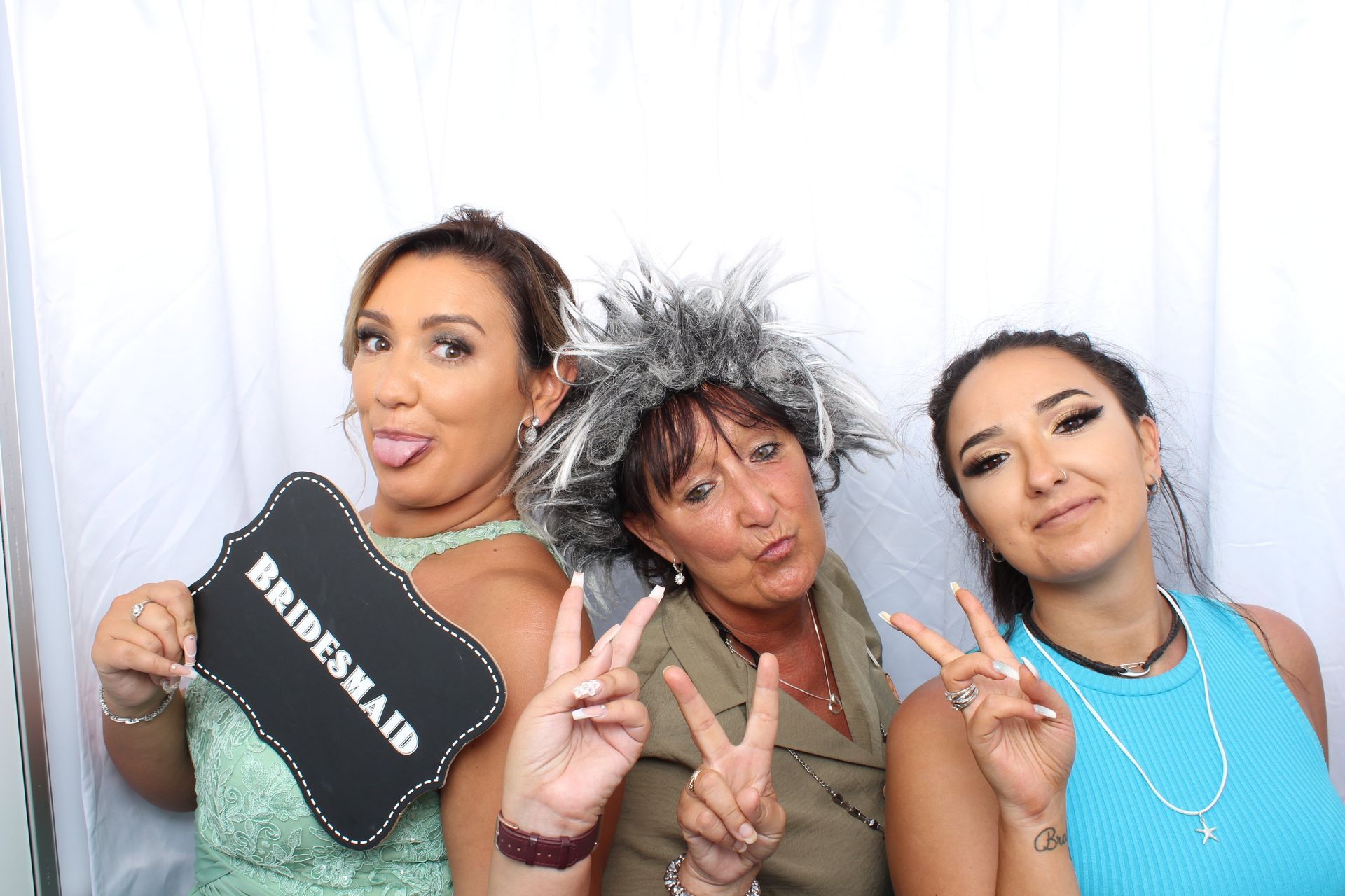 Three people in a photo booth pose with hand signs and a 