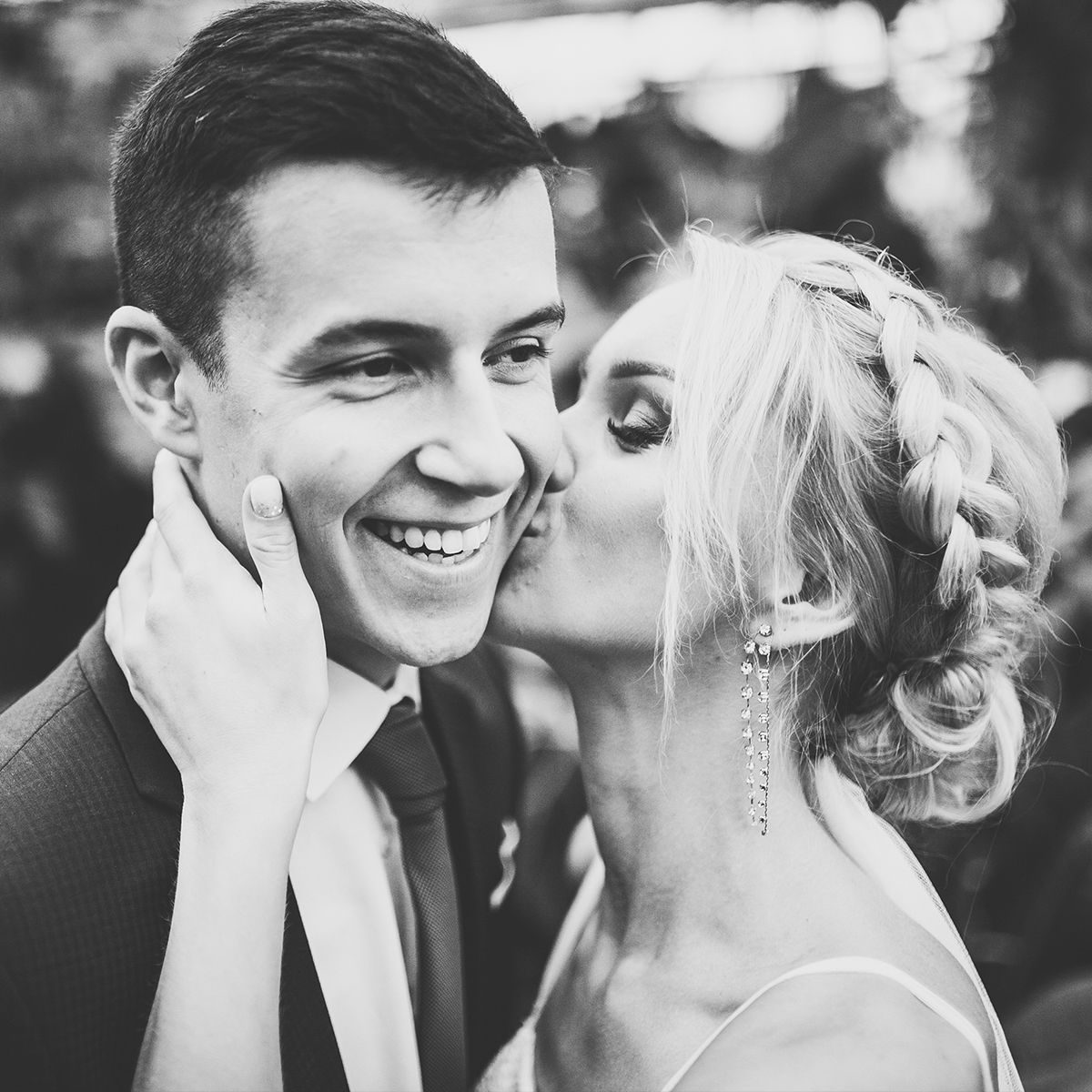 A black-and-white close-up of a person kissing their partner on the cheek; the partner is smiling warmly.