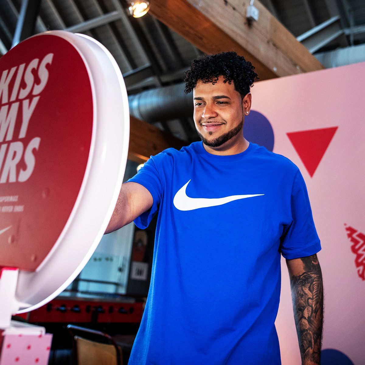 A person in a blue Nike t-shirt smiles while touching a round red sign that says 