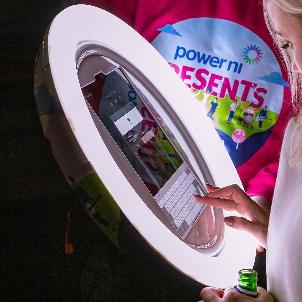 A person uses a round, illuminated digital photo booth touch screen at a Power NI event.