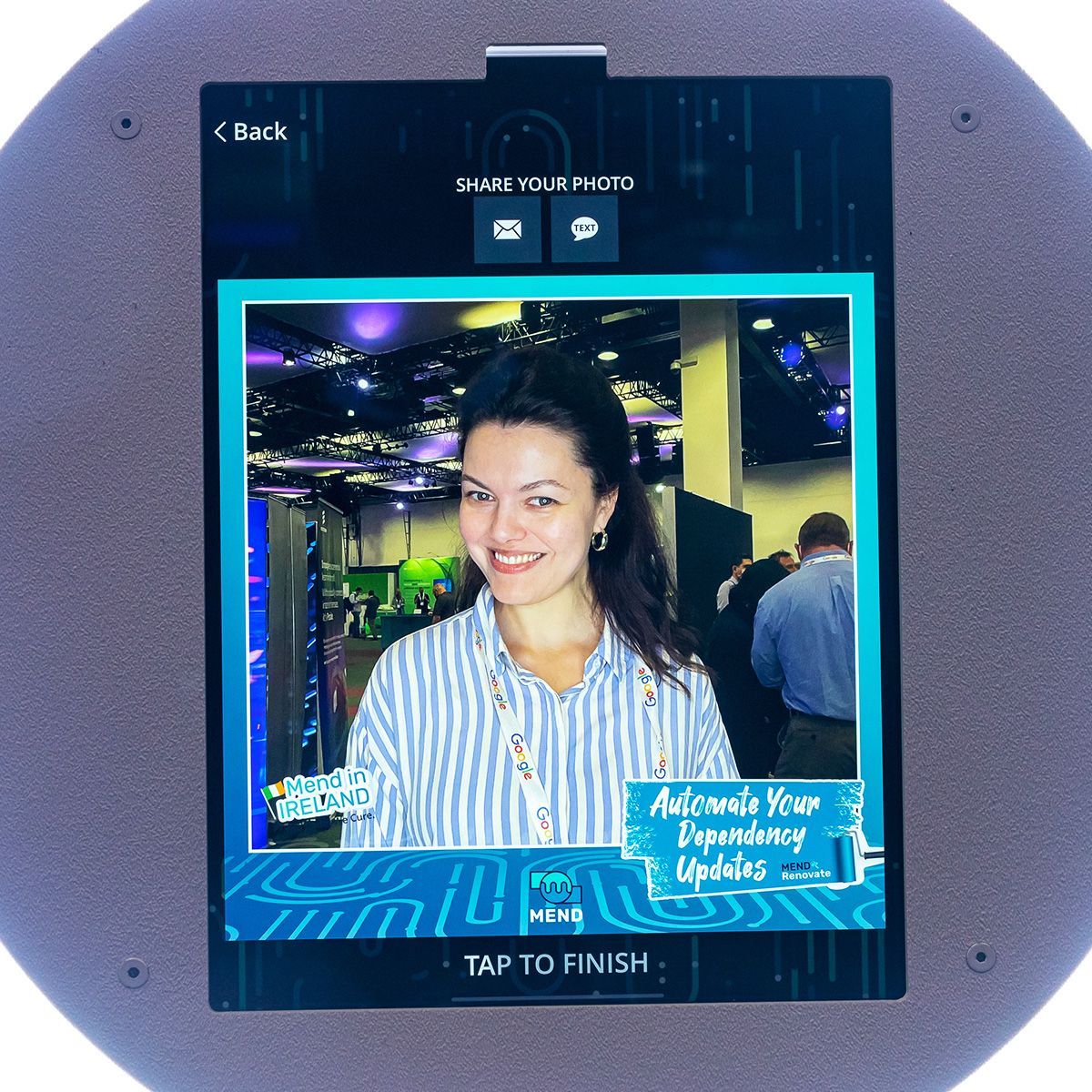 A screen shows a photo of a person smiling at a conference with event branding, offering options to share the image.