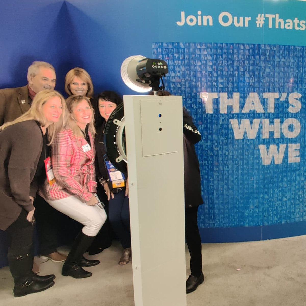 A group of people poses for a photo in front of a blue wall featuring the hashtag text #ThatsWhoWeAre.