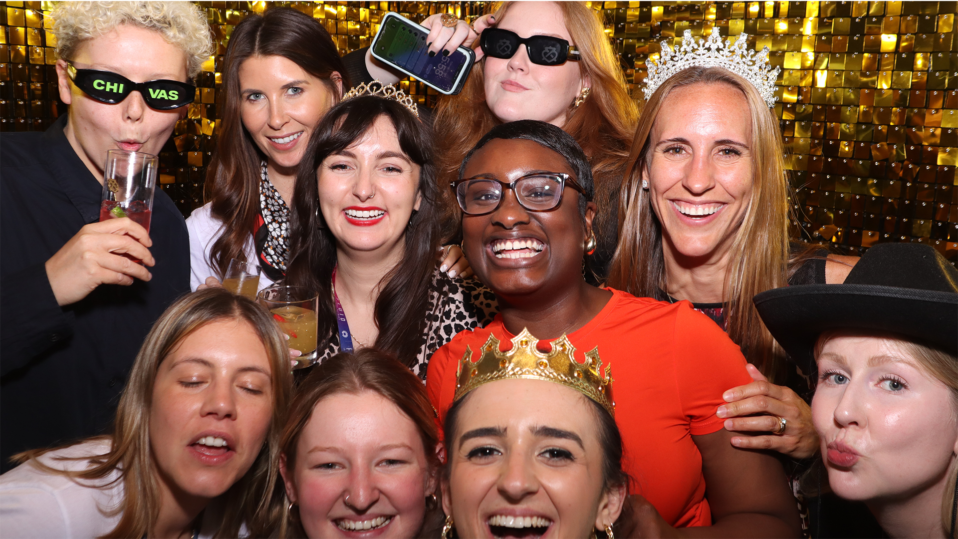 A group of friends smiling and posing together in a photo booth with gold lights in the background.