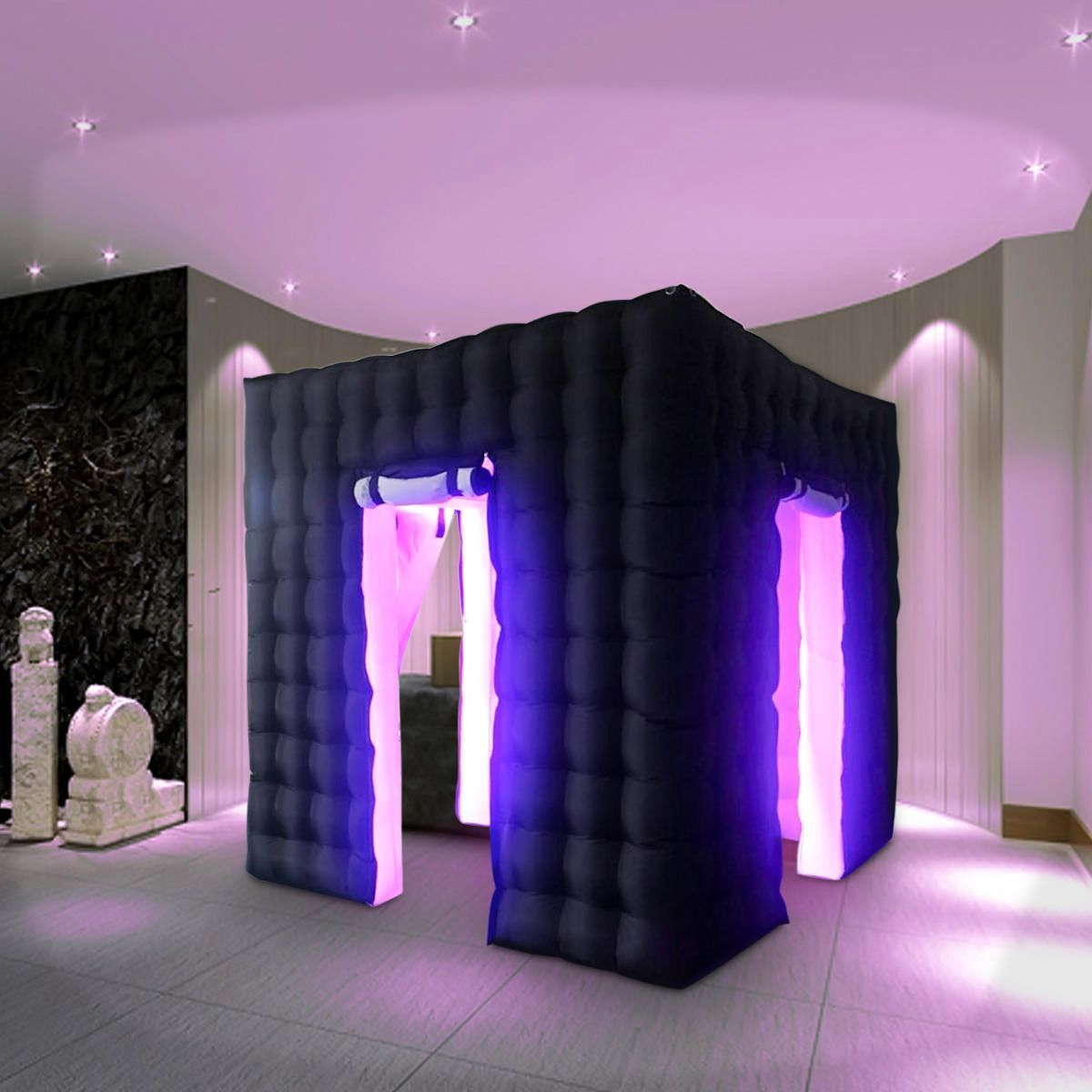 An inflatable, dark-colored cubic photo booth structure with glowing purple LED light pillars in a modern, lit room.