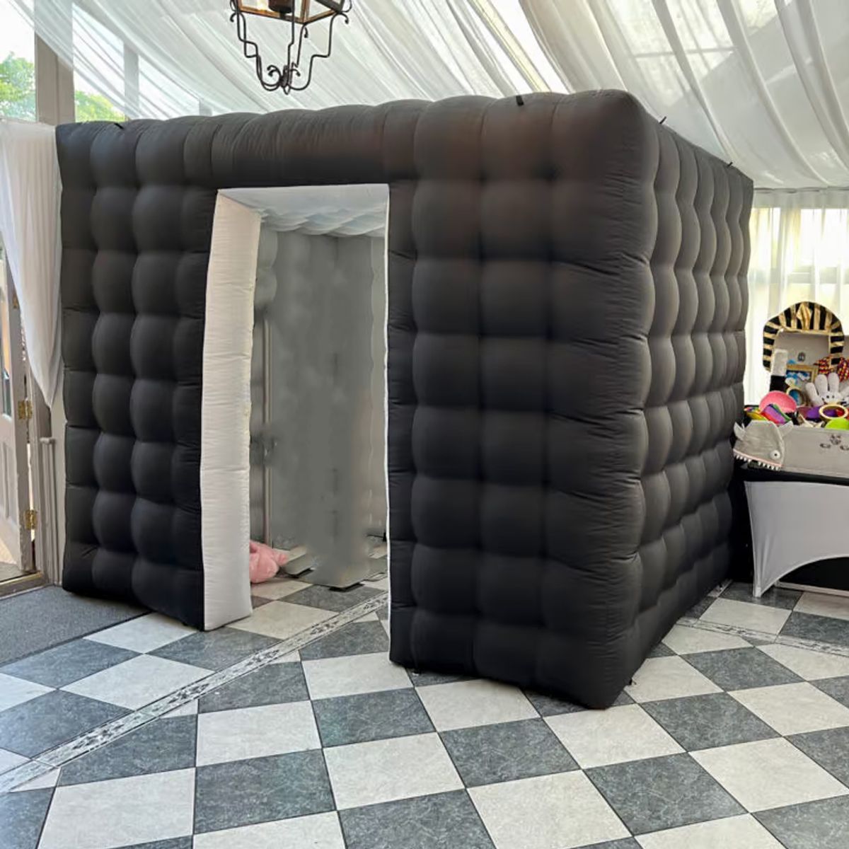 An inflatable black photo booth with a square tufted design stands on a gray and white checkered tile floor.