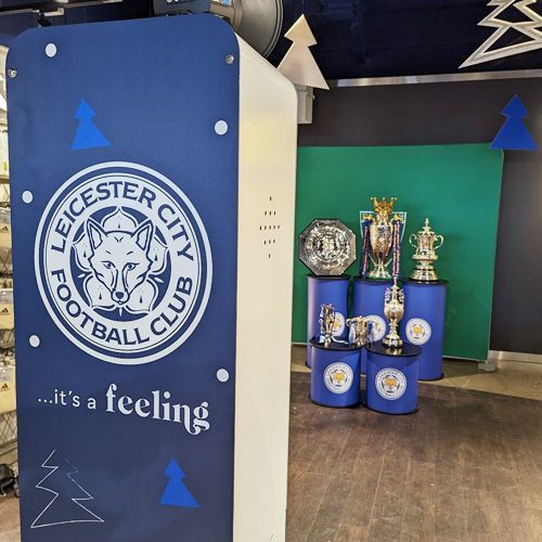 A display of Leicester City FC trophies, including the Premier League trophy, arranged on blue stands in a store.