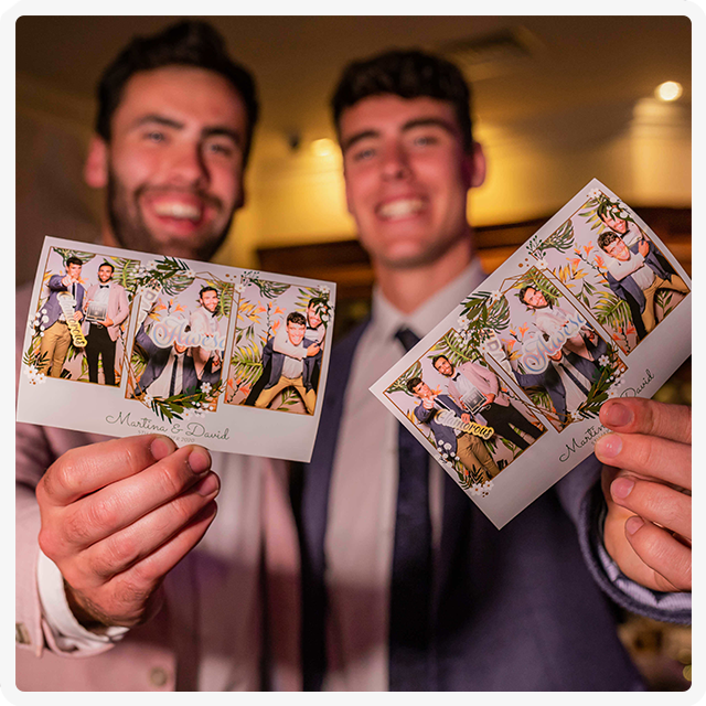 Two smiling people hold up photo booth strips showing fun poses at an evening event.