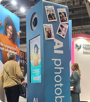 An AI photo booth tower at a conference, featuring a touch screen, top camera, and printed sample photos.
