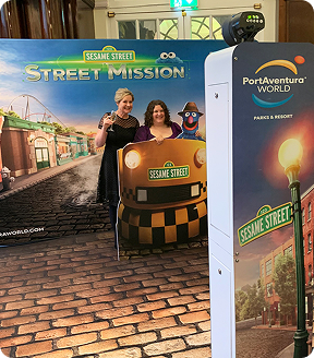 Two women pose behind a Sesame Street taxi cutout at a PortAventura World branded photo booth event.