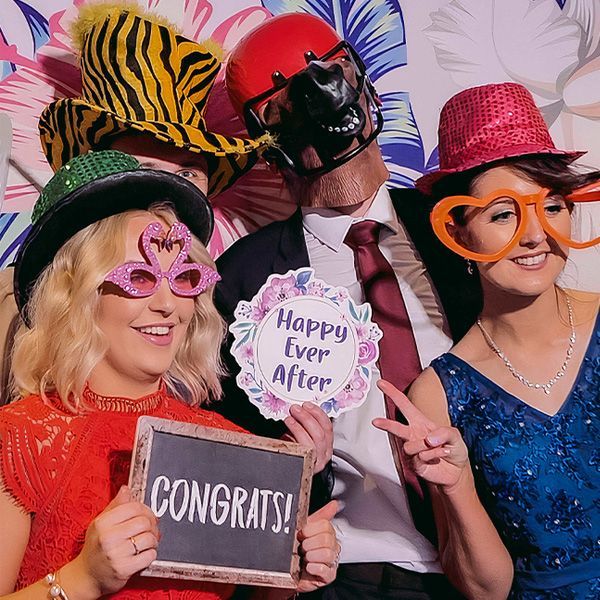 Three people wearing playful hats and props pose for a photo with signs saying