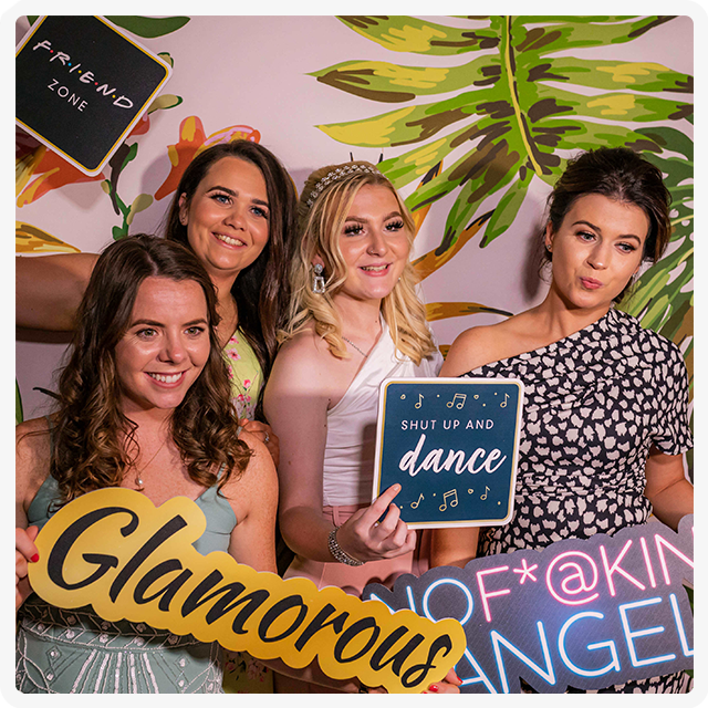 Four people pose for a photo in front of a tropical-themed wall, holding signs that say 