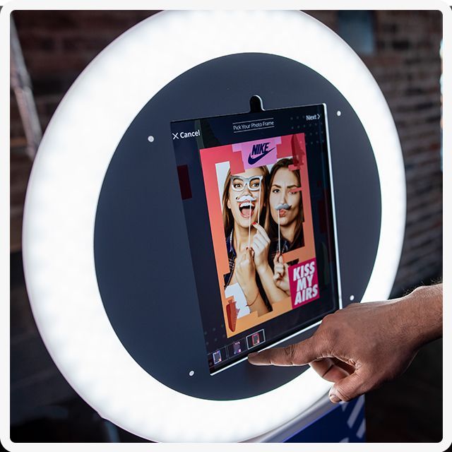 A person uses their finger to select an option on a glowing, circular ring light photo booth displaying a Nike graphic.