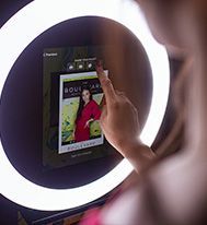 A person touches a digital screen on a ring light photo booth displaying a magazine-style photo template.