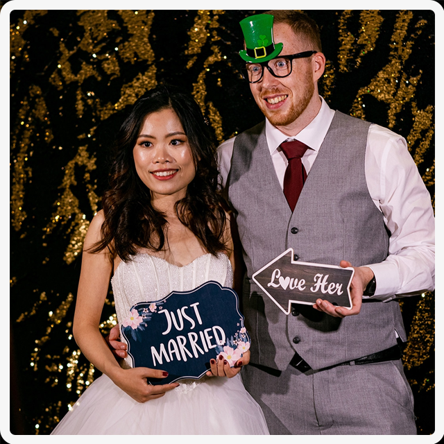 A couple at a wedding photo booth, holding signs that say 