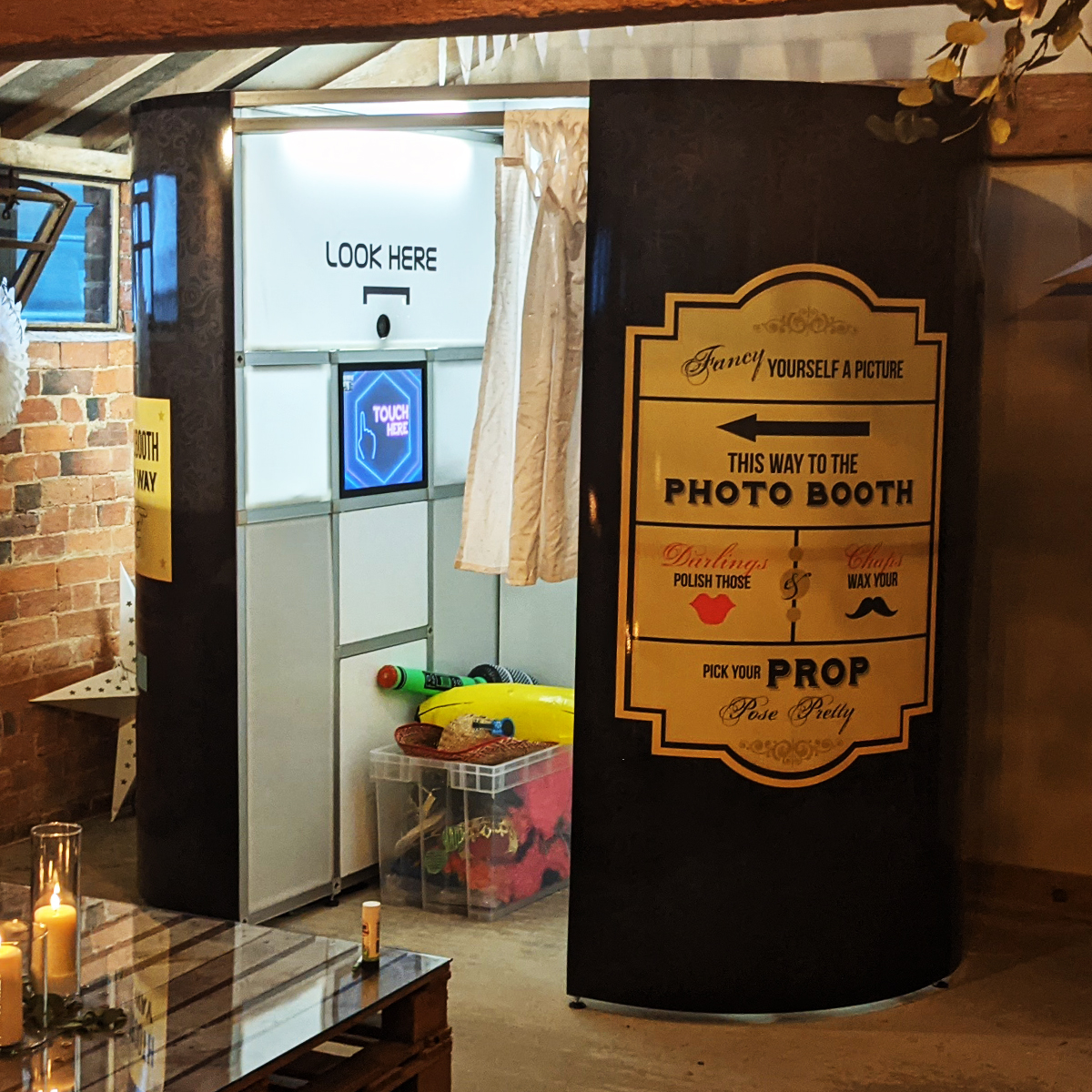 A black photo booth with a sign pointing the way, next to a clear bin filled with various colorful props.