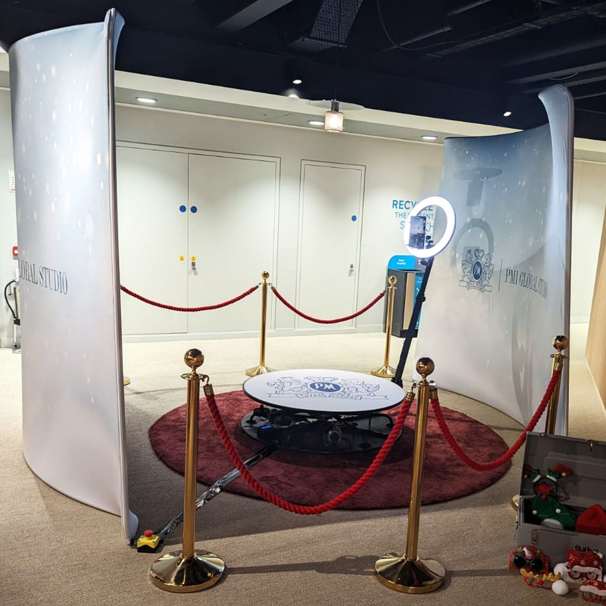 A 360-degree photo booth with a rotating arm, ring light, and stanchions on a red circular rug within a display area.