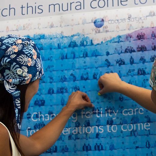 Two people place stickers on a blue wall mural titled