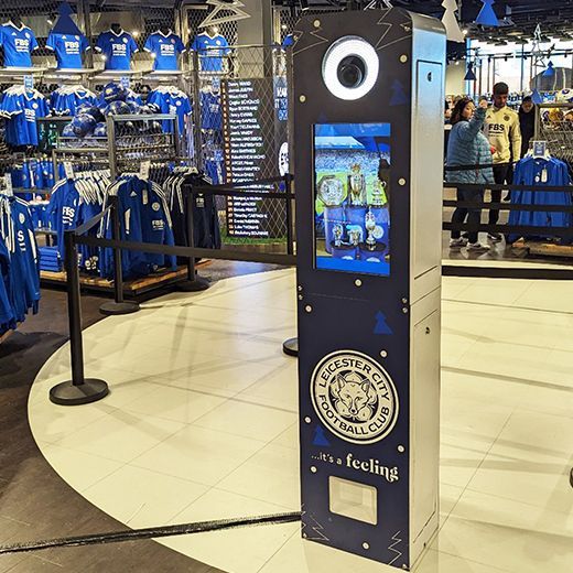 A Leicester City Football Club branded photo booth kiosk stands in a retail store filled with blue team jerseys.