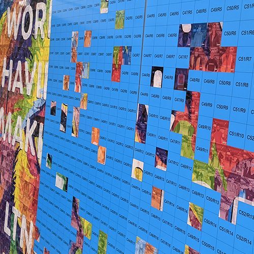 A blue grid wall displaying various small, colorful square art pieces or photos arranged in a scattered pattern.