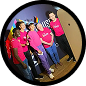 Five people wearing bright pink shirts stand together smiling in a dimly lit, indoor space.