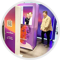 A person stands near a branded, purple-to-orange Accenture photo booth with a QR code and a large printed face graphic.