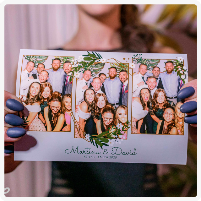 A person holds a photo booth strip from Martina and David’s wedding featuring three photos of guests posing together.