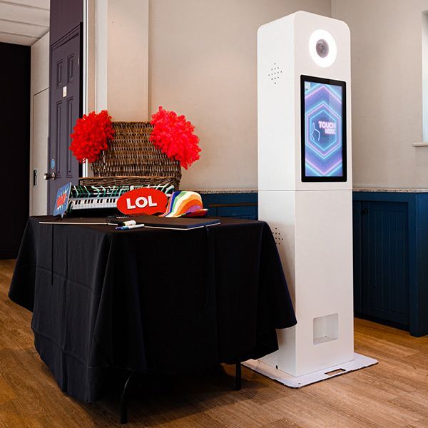 A white photo booth stands next to a black-covered table holding party props, including red fans and an