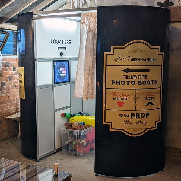 A black photo booth with a side sign directing guests to 