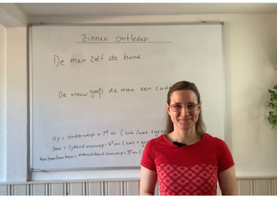 Een vrouw staat voor een whiteboard in een klaslokaal en lacht naar de camera.