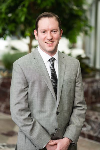 A man in a suit and tie is standing in front of a tree.