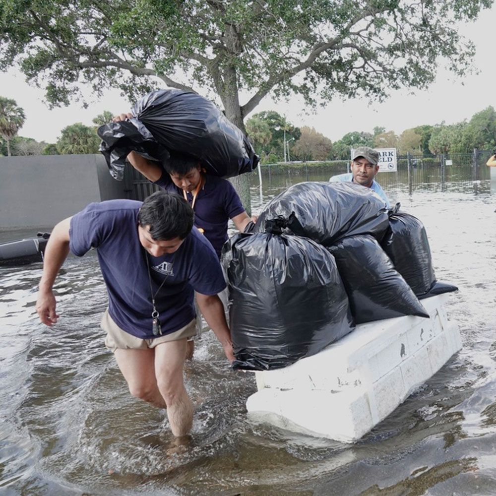 FEMA Two men are carrying bags of trash through a flooded area