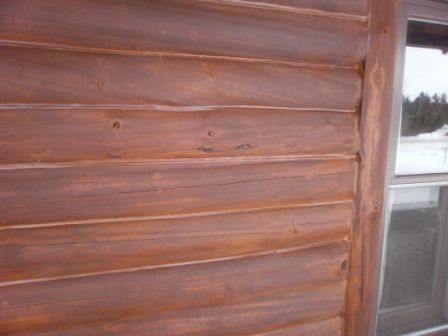 Brown stained log cabin exterior, with window on the right side.
