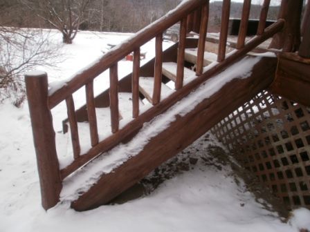 Snowy wooden outdoor staircase with handrail and railing.