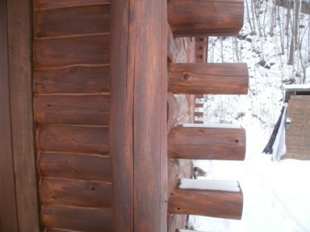 Close-up of a wooden cabin exterior with logs. Brown color and snow in the background.
