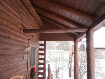 Wooden porch with log beams and columns, overlooking a snowy outdoor scene.