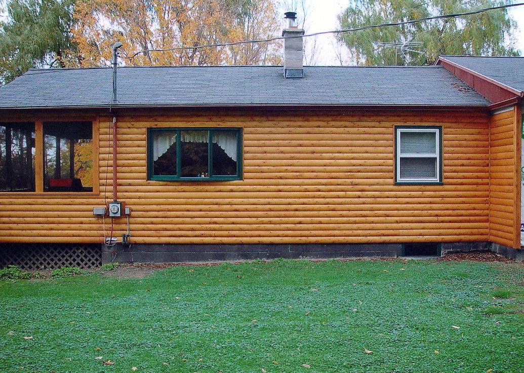 Yellow log cabin with a green window frame and gray roof, set in a yard with green grass.