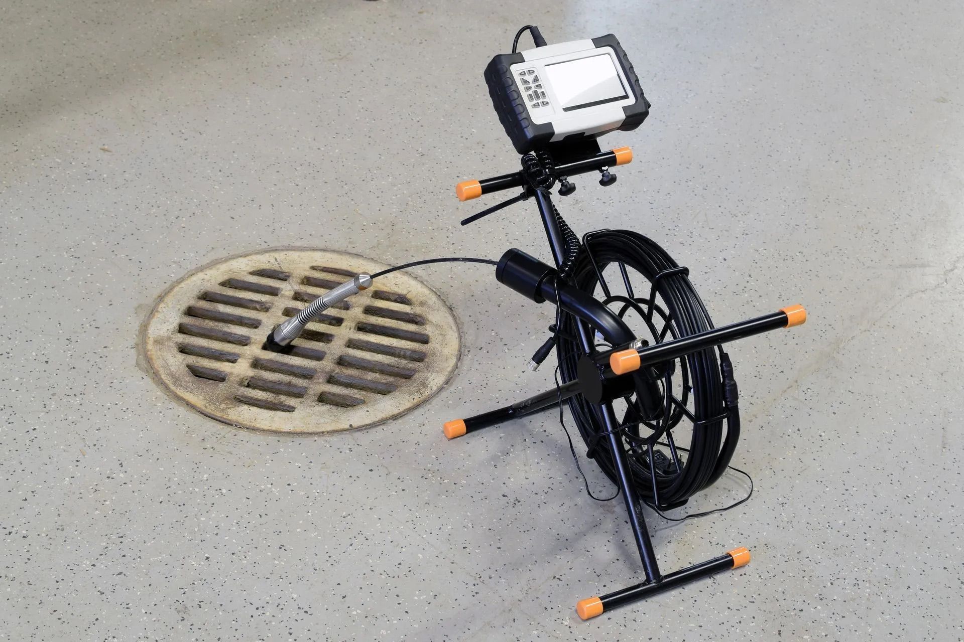 Une caméra d'inspection des égouts avec un écran, montée sur un support en métal noir, placée à côté d'une bonde circulaire au sol.