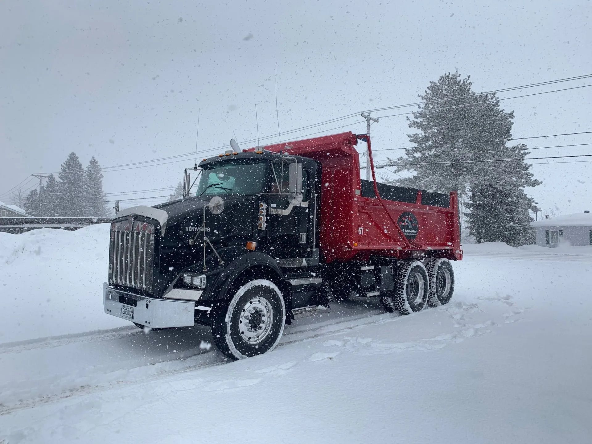 Un camion-benne noir et rouge stationné sur un terrain enneigé pendant une chute de neige.