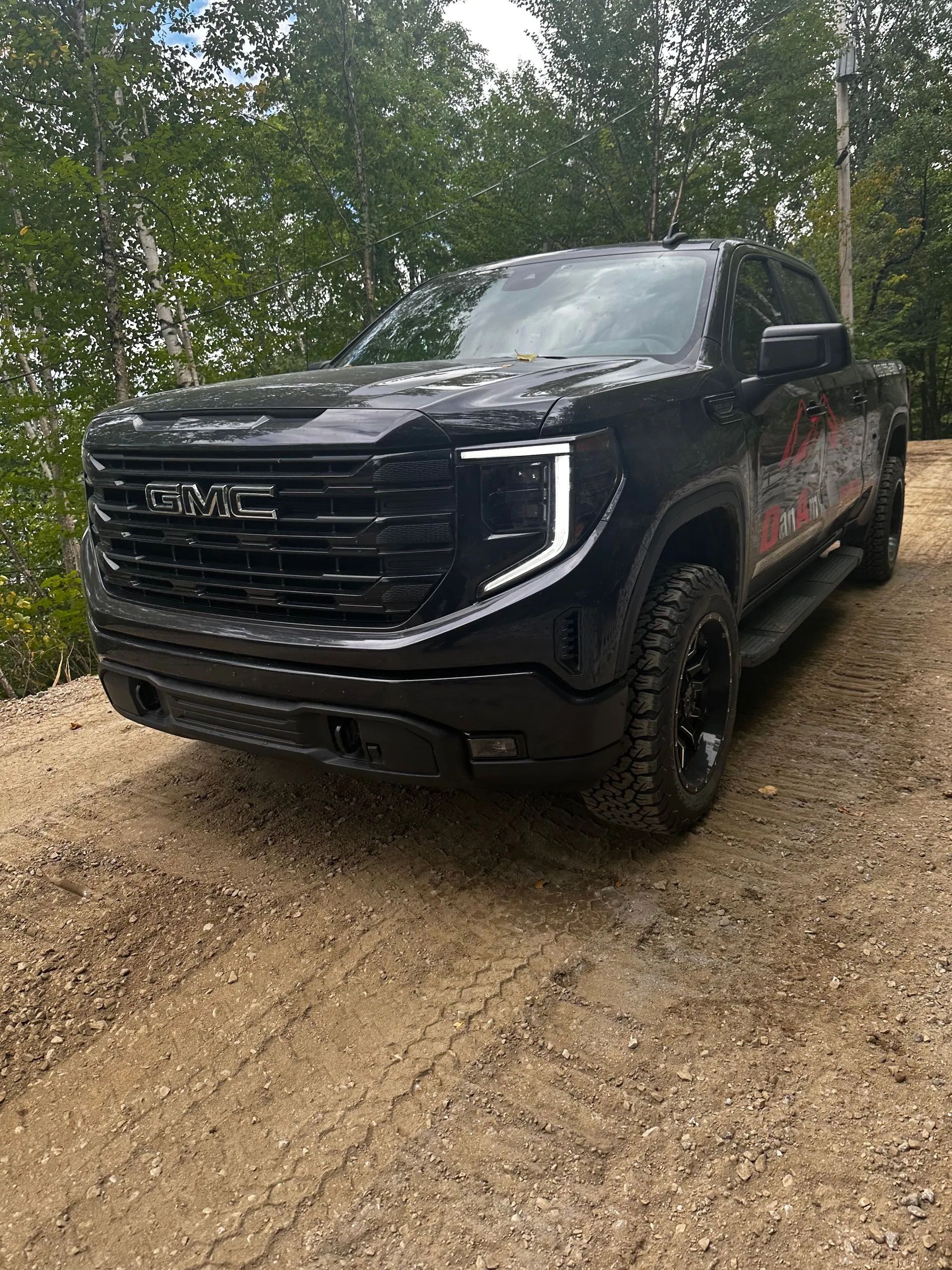 Un pick-up GMC Sierra noir garé sur un chemin de terre, avec des arbres en arrière-plan.