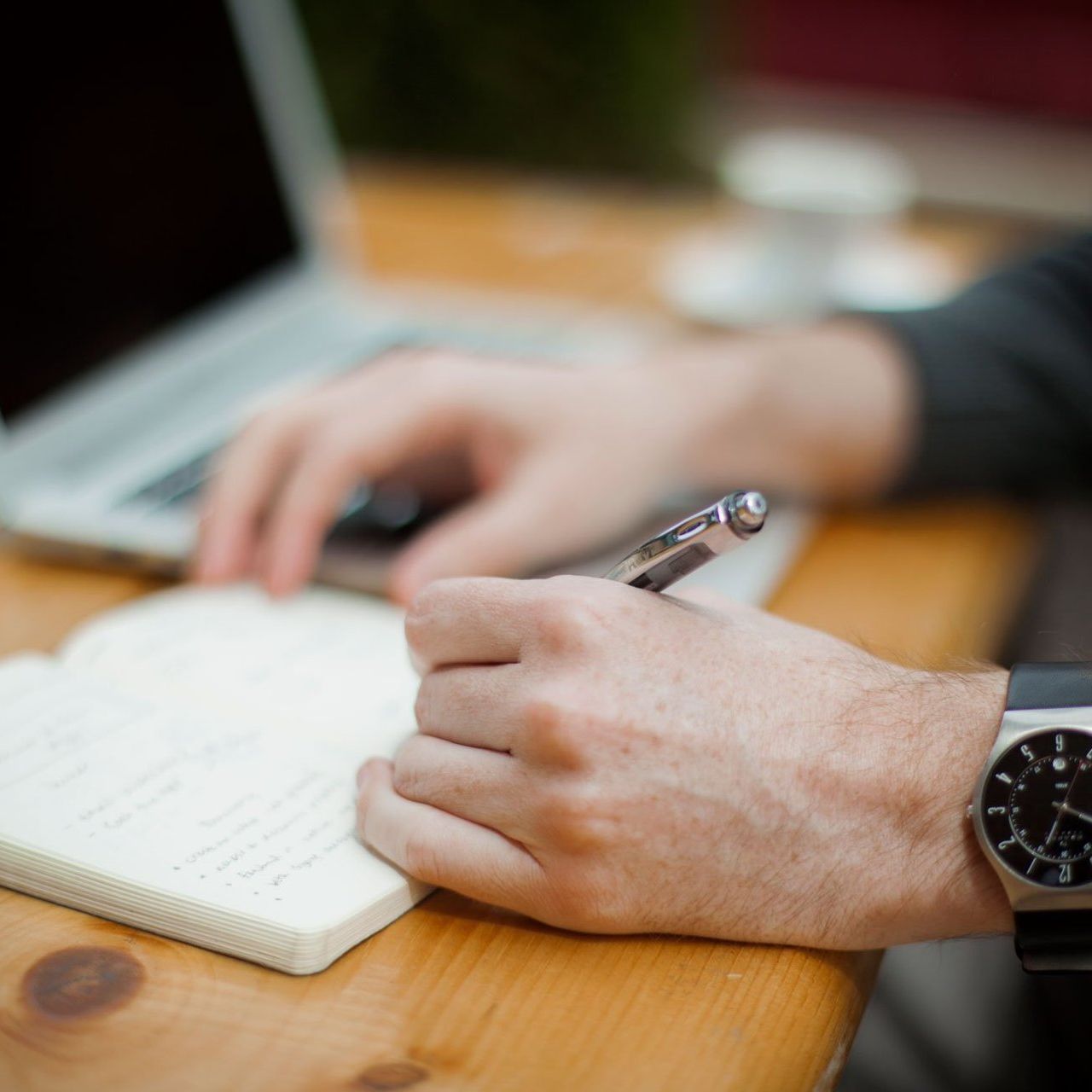 A person wearing a watch is writing in a notebook