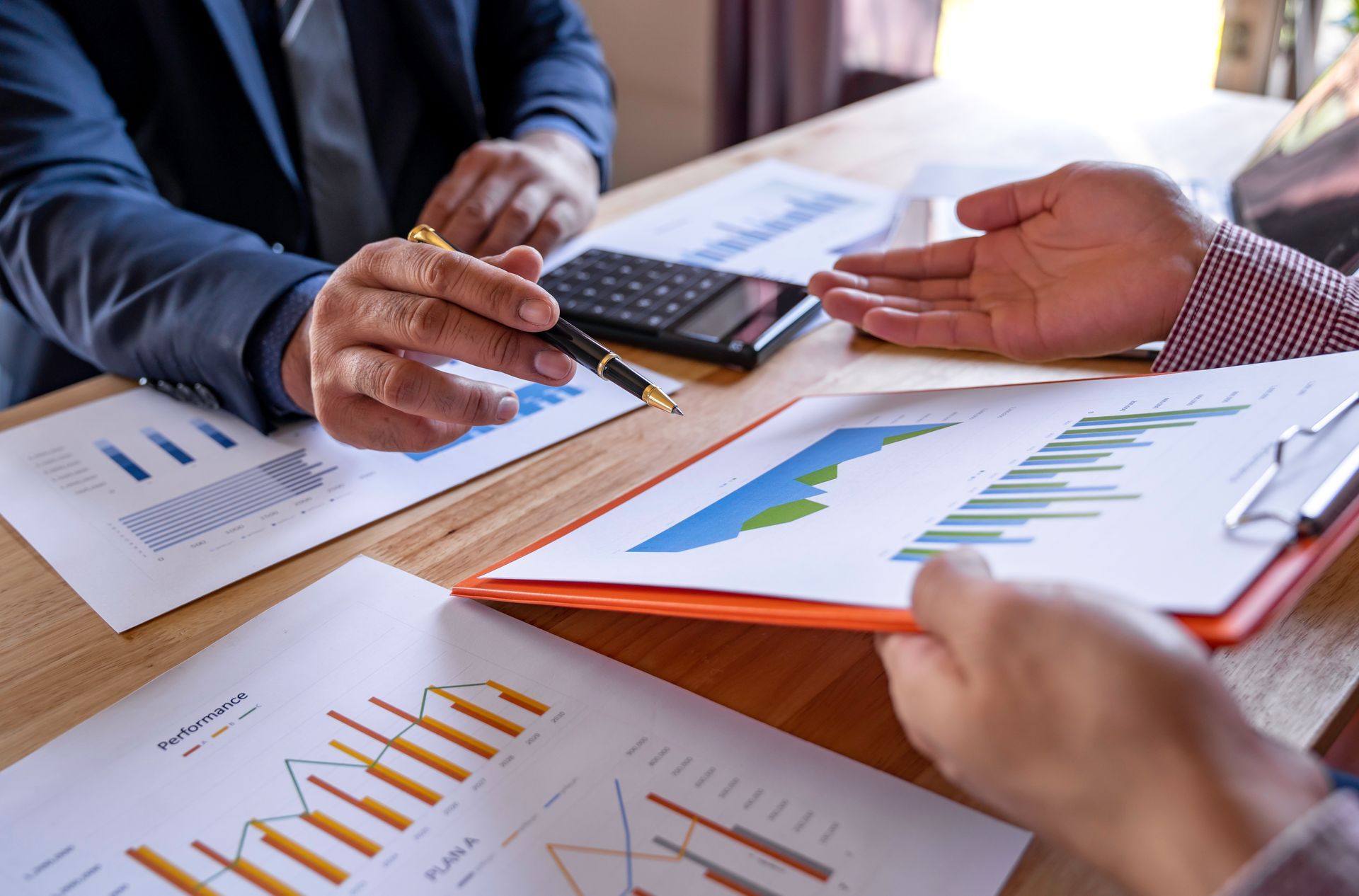 Two men are sitting at a table with papers and a calculator.