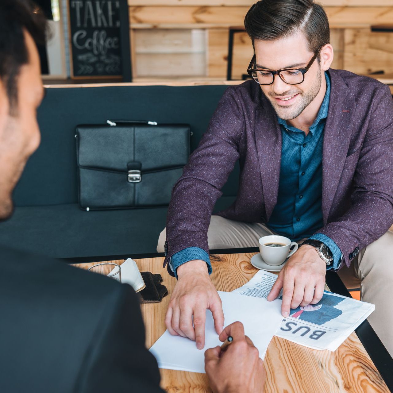 Two men are sitting at a table with a sign that says take coffee