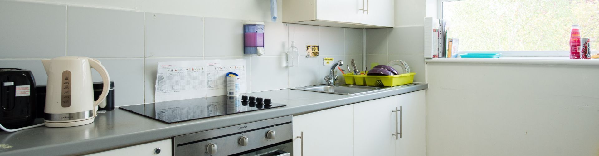 a kitchen with white cabinets , a stove , a kettle , and a sink .