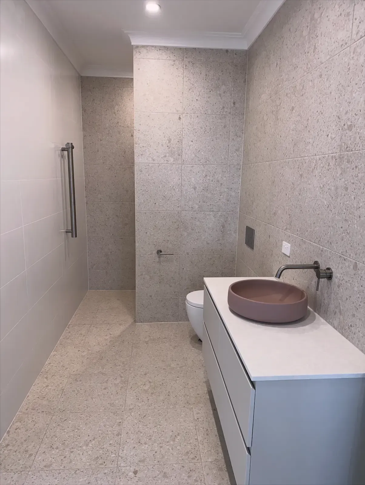 Modern bathroom with speckled stone walls, white vanity, and a round vessel sink.