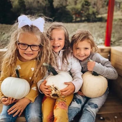 Three little girls are sitting on a bench holding pumpkins.