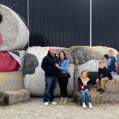 A family is posing for a picture in front of a large bale of hay.
