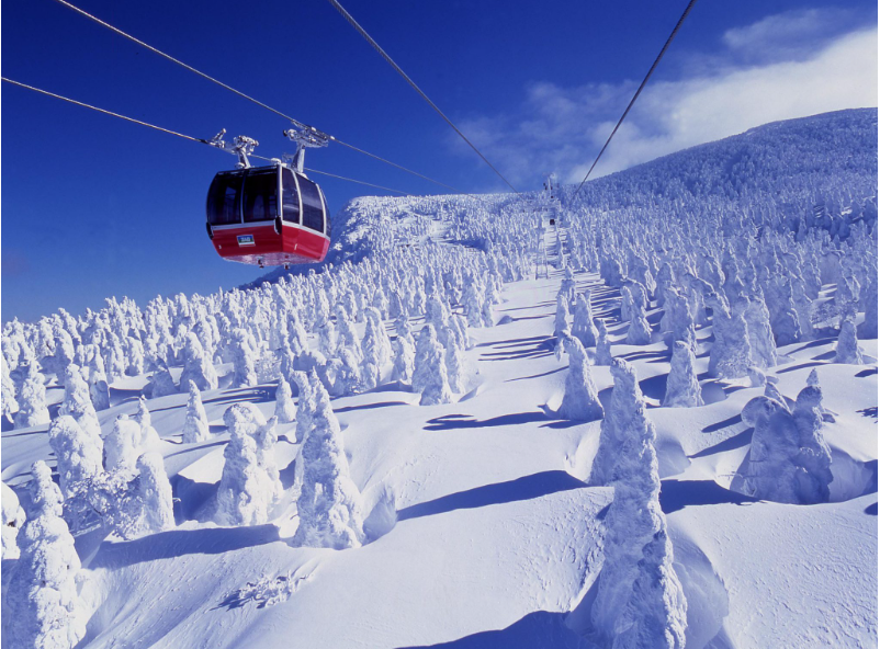 Red gondola cable car over snowy mountain forest under clear blue sky